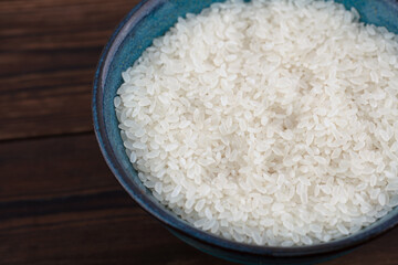 A bowl of raw white rice on a wooden table