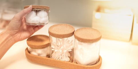 The female hand opened the glass bottle with the cotton pad inside to remove the makeup put on the table in the bedroom.
