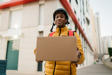 Smiling black delivery man giving parcel to camera