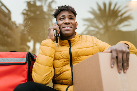Positive delivery man with box talking on cellphone