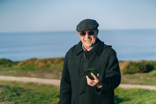 Cheerful mature man browsing smartphone on seashore