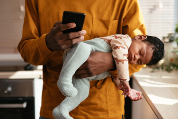 Crop dad with sleeping baby using cellphone