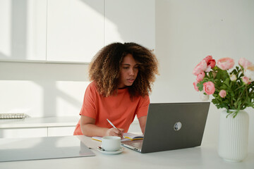 Cheerful black woman taking notes in notepad at home