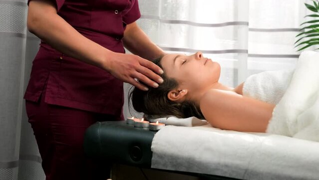 Beautiful young girl having head massage in spa salon to restore blood flow to the head and relax her body.