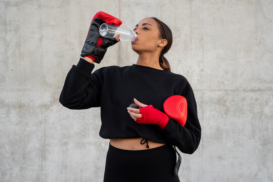 Sportswoman in boxing gloves drinking water