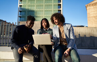 Diverse coworkers using laptop together on street