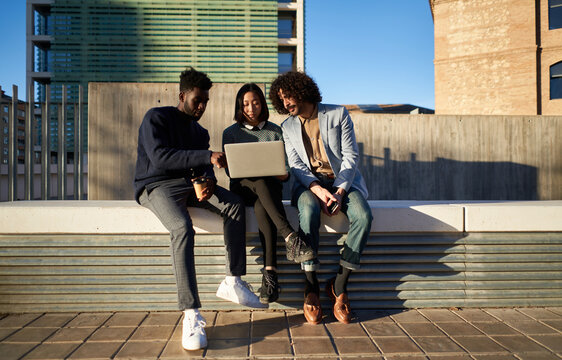 Diverse coworkers using laptop together on street