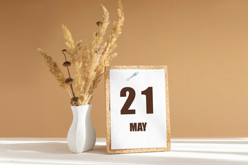 may 21. 21th day of month, calendar date.White vase with dried flowers on desktop in rays of sunlight on white-beige background. Concept of day of year, time planner, spring month