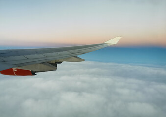 Obraz premium View from the porthole on the wing of an airplane with a red aircraft engine flying above beautiful white clouds.