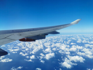 View from the porthole on the wing of an airplane with a red aircraft engine flying over beautiful white clouds and the sea.