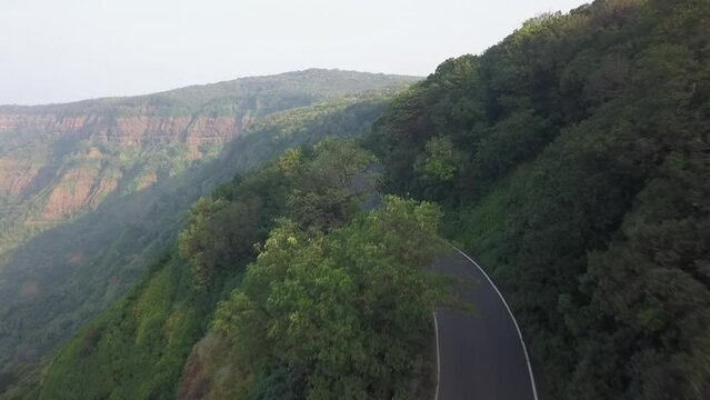 Low aerial tracks motorbike traffic on twisty mountain road in India