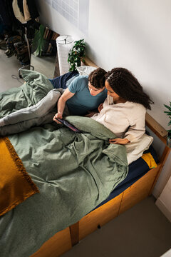 Diverse couple browsing digital tablet in bed at home