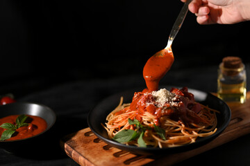 Female hand garnishing and preparing Italian pasta spaghetti with tomato sauce.