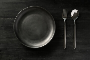 Overhead, Empty black ceramic plate with silverware on black wood table.