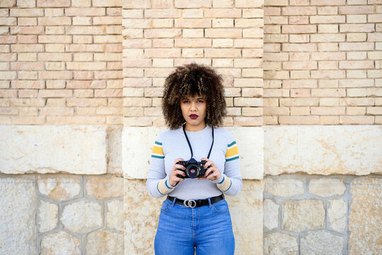 Serious woman with photo camera near brick wall