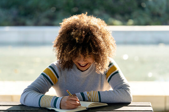 Smiling student with curly hair taking notes in notepad