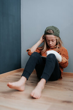 Thoughtful boy with cast on broken arm reading on a tablet