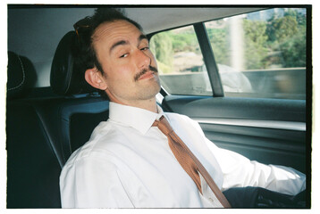 Man wearing a shirt and tie in the back of a car 