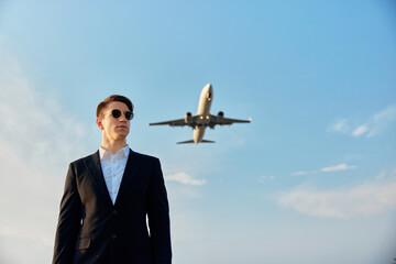 Young traveler in black suit and airplane in sky. Businessman traveling concept.