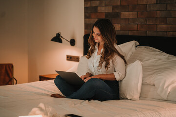 Woman sitting on bed and browsing laptop for online job