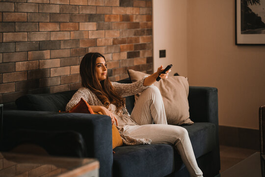 Woman sitting on couch and switching channels on TV