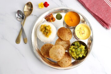 Indian vegetarian Thali or platter includes Aloo ki sabji, dal rice, Puri bhaji, Shrikhand or Srikhand, Aamras, papad, pickle, and chutney. Indian food is served in a Silverplate or thali. Copy Space.