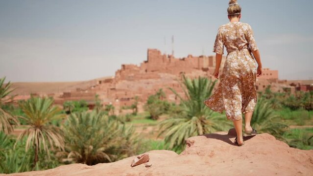 Slo Mo: Woman in floral dress looks at fortified village in morocco