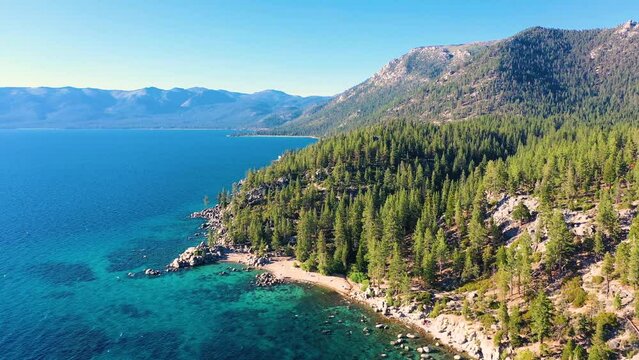 Aerial Drone View of Lale Taho Mountains And Thick Pine Tree Forest In The Sierra Nevada with Crystal Clear Blue Water And Beach With Boulders And Rock Jetty