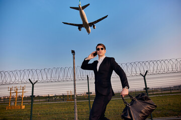 Young traveler in black suit and airplane in sky. Businessman traveling concept.