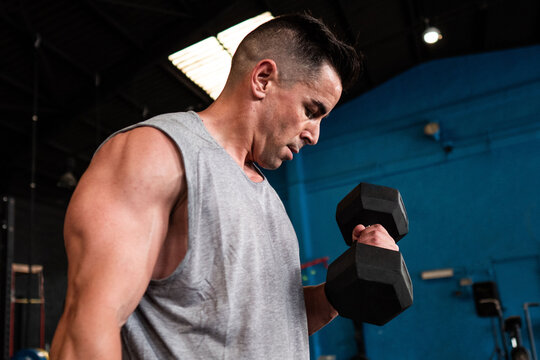 Serious muscular man exercising with dumbbell