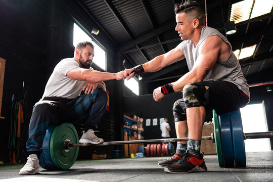 Strong athletes sitting on barbell and bumping fists
