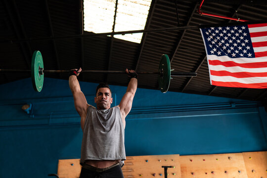 Muscular guy lifting barbell in modern gym