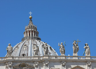 Fototapeta na wymiar Statue of Resurrected Jesus and more statues on the facade of the Basilica of Saint Peter in Vatican and the dome in background