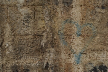 Faded graffiti of a blue heart on an ochre stone wall