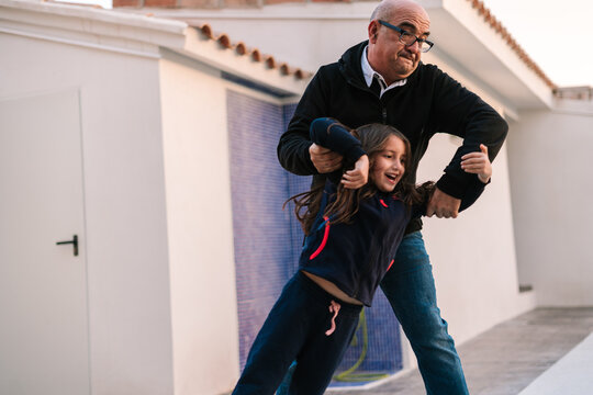 Senior Grandfather Lifting Heavy Smiling Girl On Yard