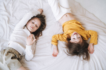 Cute little sisters girls on having fun on bed at the home, top view
