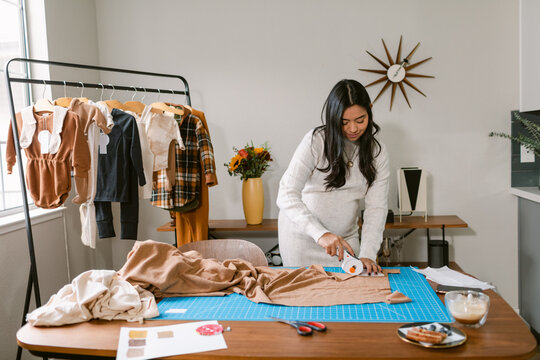 Pregnant dressmaker cutting fabric in apartment