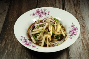 Traditional fresh lotus root or stem salad mixed with fish pickled sauce and shallot serving on the plate. Famous street food menu in Thailand. 