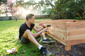 Man With Drill Building Raised Garden Beds in Backyard