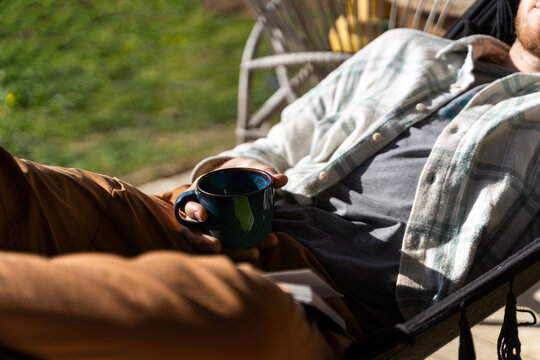 detail of Young man relaxing and sunbathing on hammock having coffee