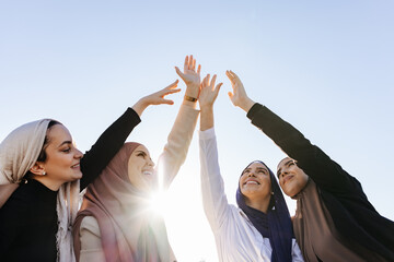 Cheerful Muslim women in hijab clasping hands in the air