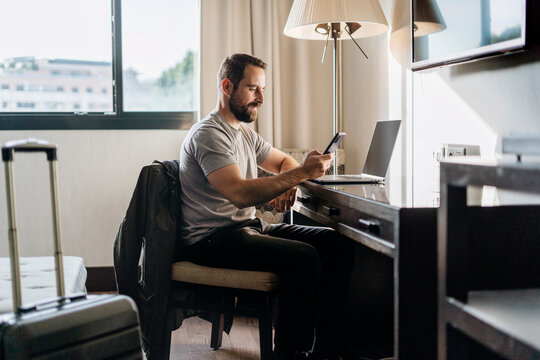Adult man browsing smartphone and working on laptop