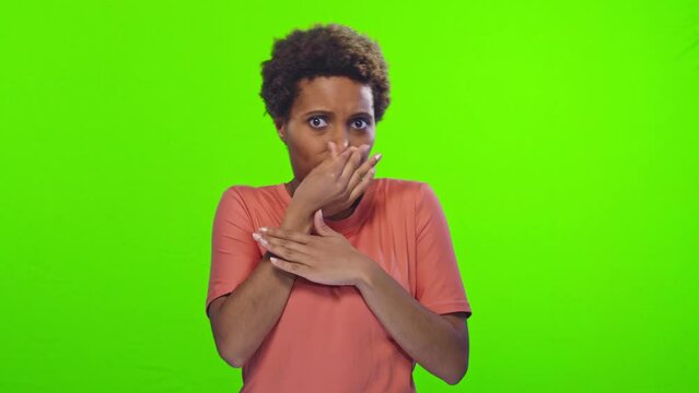 Young funny short haired African American woman with bulging eyes feels bad odor from something closes nose and waves hand to disperse stench is disgusted stands in studio on green background