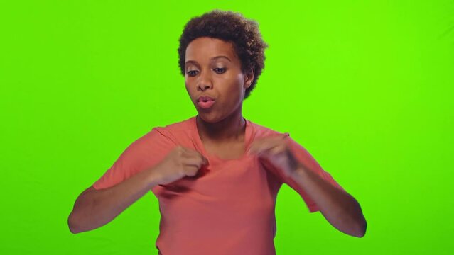 Young attractive African American woman suffering from sweltering weather and hot summer breathing deeply fanning himself with hands dressed in casual T-shirt stands in studio on green background