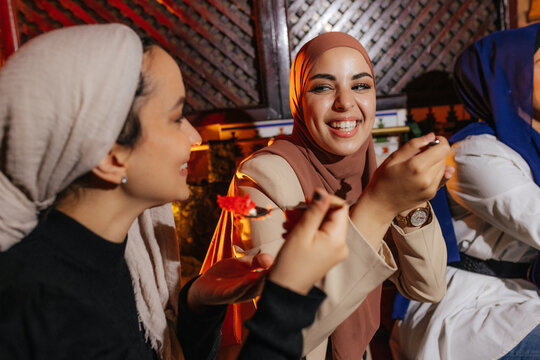 Happy Muslim women in hijab eating red velvet cakes in tea house