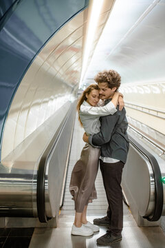The guy gently hugs his girlfriend near the travolator
