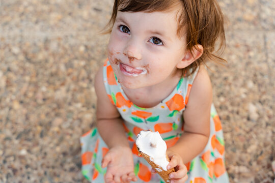 Happy little girl eating ice cream with dirty face in summer
