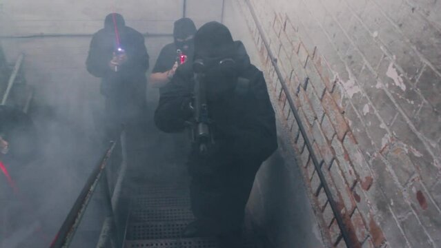 A special forces swat team ascends a stairwell with guns and laser sights wearing balaclavas and gas masks