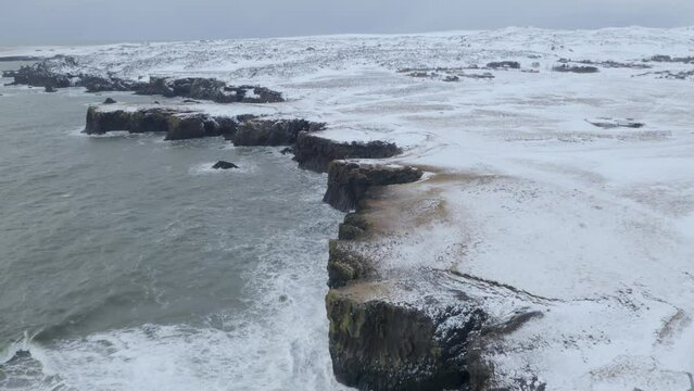 Arnarstapi Village In Snaefellsnes With A Beautiful Coastline And Gatklettur At Wintertime In Iceland. - aerial pullback