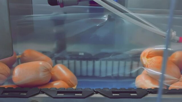 Industrial meat processing plant factory. Boiled sausage semi-finished products are on production line for vacuum packaging food in plastic on conveyor belt in workshop. Polyethylene film